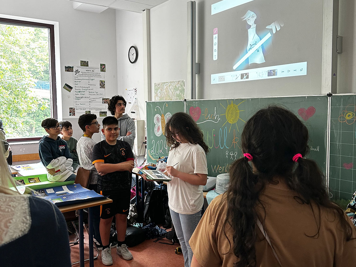 Schülerin mit Tablet und Beamer und andere Schüler und eine Lehrkraft stehen daneben