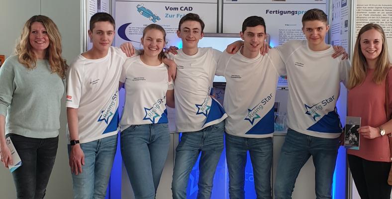 Die Mitglieder des Teams Rising Star mit Frau Spaller und Frau Mohner vor ihrem Boxenstand auf der NRW-Meisterschaft des Wettbewerbs Formel Eins in der Schule.