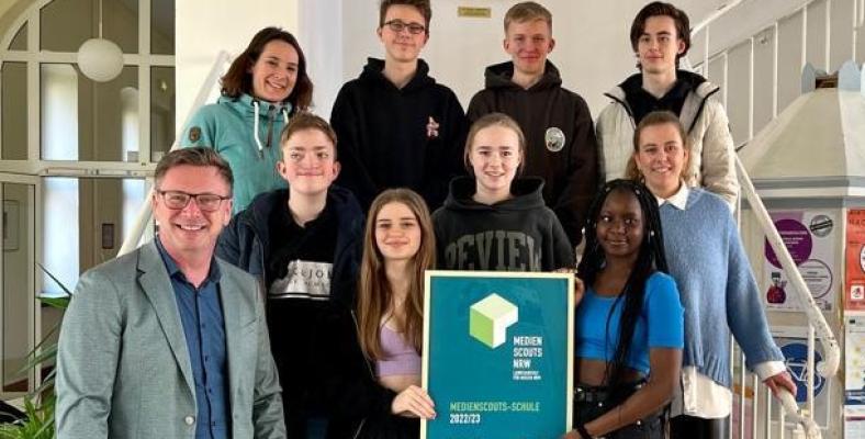 Die Medienscouts präsentieren zusammen mit Schulleiter Christian Fischer (v.l.), Alexandra Löpke (o.l.) und Pascalina Tophoven (m.r.) die Auszeichnung Medienscouts-Schule 2022/23.
